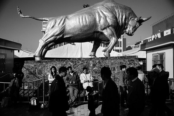 Travelers walk past a large bull sculpture outside the Kunming Railway Station in Kunming, Yunnan Province, China. Travelers walk past a large bull sculpture outside the Kunming Railway Station in Kunming, Yunnan Province, China.