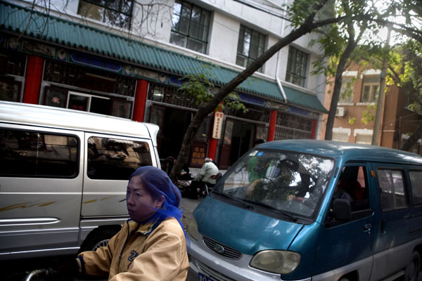 msb-116630mod A woman wearing a scarf over her face rides a bicycle on a street in Tianjin, China.