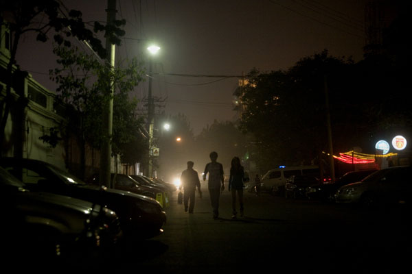 msb-116830mod People illuminated by the lights of a car walk down a street in Tianjin, China.