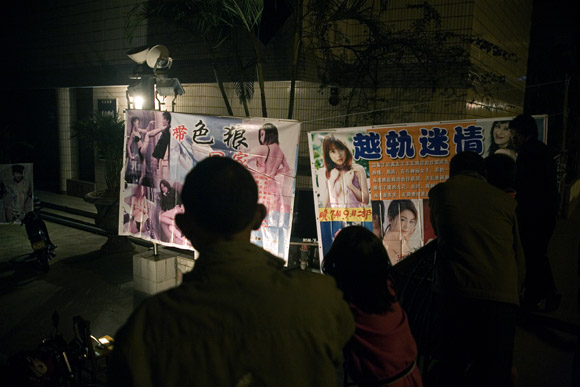 Men look onto a brothel with advertisements and posters showing naked women in Hekou, Yunnan Province, China, on the Vietnam border.