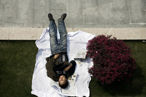 A man sleeps on grass in People's Park in central Shanghai, China.  People's Park is known as Renmin Park or Renmin Guangchang in Mandarin chinese.