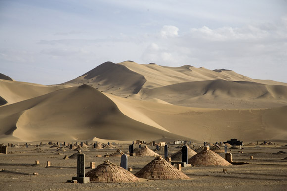 A cemetery stands beneath dunes of the Gobi Desert near Dunhuang, Gansu, China.  An area of the desert near this dune will be the site of the world's largest solar power generating field. The desert and surrounding areas is closely protected and managed by the local government, but ethnic groups have been given special permission to use the desert according to their traditions.