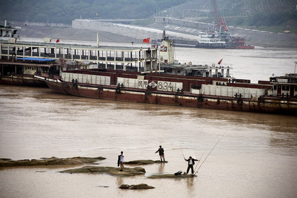 Men fish in the Yangtze River as barges pass by Chongqing, China. Increased river traffic and nearby manufacturing in the area has threatened the river's long-term ecology.
