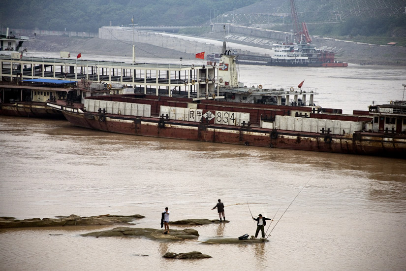 Men fish in the Yangtze River as barges pass by Chongqing, China.