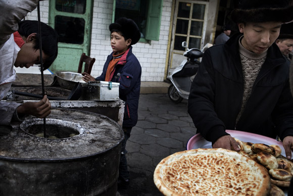 Uighur men bake flat bread (nan) in a barrel oven in the Old City section of Kashgar, Xinjiang, China.
